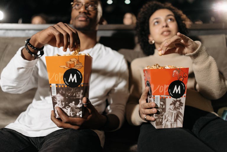 A couple enjoys popcorn while watching a movie in a theater.