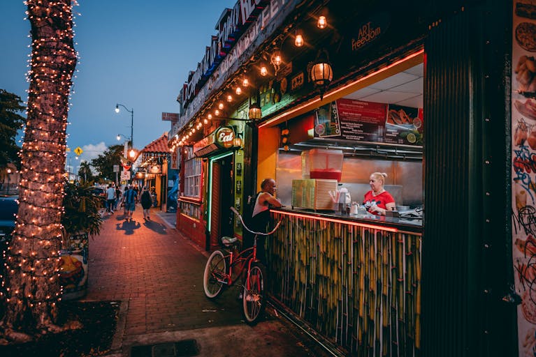 Bustling Miami street at night with a lively food stall and colorful lighting.