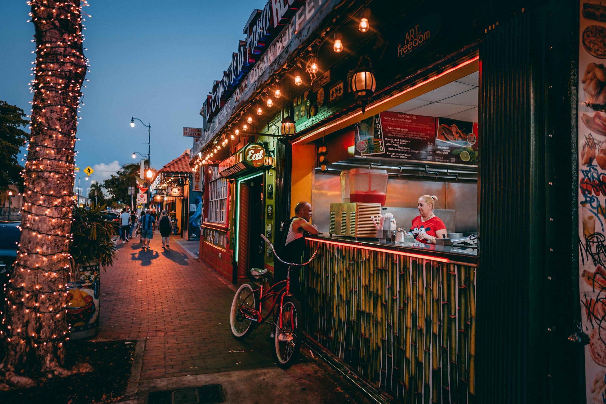 Bustling Miami street at night with a lively food stall and colorful lighting.