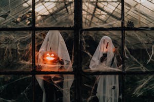 Spooky ghosts with carved pumpkins inside a spiderweb-filled greenhouse, perfect for Halloween.